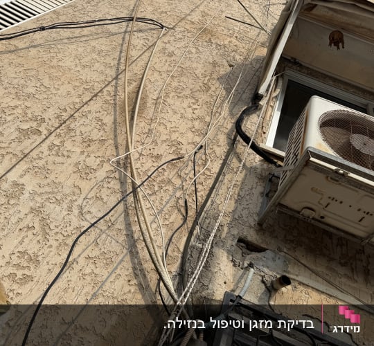 יחידת מזגן חיצונית על קיר עם חוטים חשופים